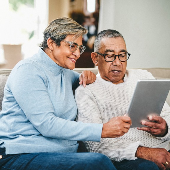 Two people sitting together on a couch looking at a silver computer tablet