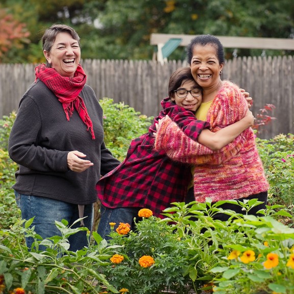 Two people hugging in a garden with another person standing next to them