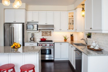 A kitchen with white cabinets and walls, two red stools, a refrigerator, dishwasher and stove