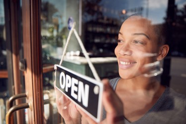 A person inside a store with their hands on an Open/Closed sign